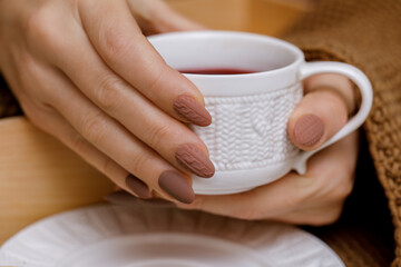 Fototapeta na wymiar Stylish winter nail design. Knitted fabric texture on women's nails. A woman's hand holds a cup of warm drink.