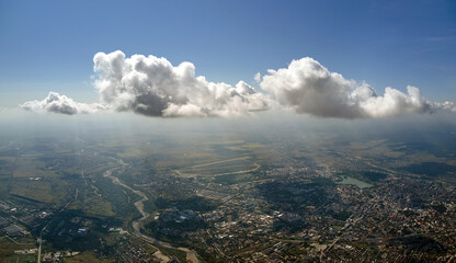 Aerial view from airplane window at high altitude of distant city covered with white puffy cumulus...