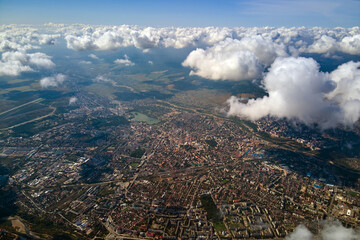 Aerial view from airplane window at high altitude of distant city covered with white puffy cumulus...