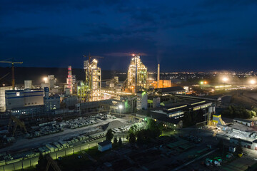 Aerial view of cement factory with high concrete plant structure and tower cranes at industrial production area at night. Manufacture and global industry concept