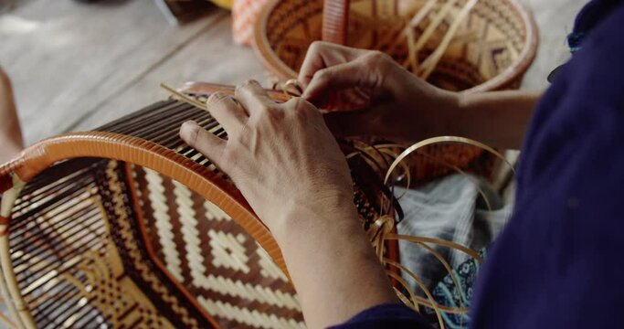 2 Thai female farmers weave basket in traditional Thai art patterns to sell as extra income in countryside of Thailand.	