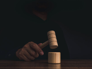 A wooden judge gavel in hand with the soundboard on a wooden table on dark background. Man in black...