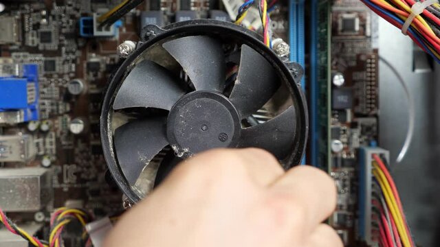 unrecognizable master cleans a fan of a disassembled dusty computer with a cotton swab, close-up.
