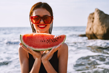 cheerful woman in sunglasses eating watermelon by the ocean