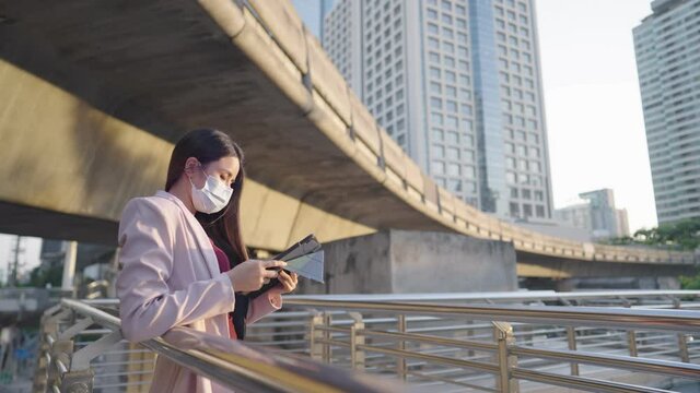 Attractive business woman leaning on metal handrail on walking bridge with hand using on a digital tablet, convenience wireless device for outside working, an online working technology innovation