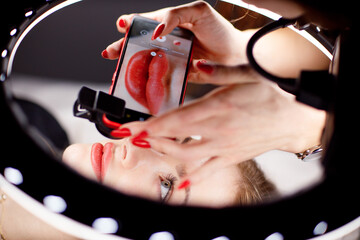 Cosmetologist making photo of work on mobile phone red permanent make up tattoo on young woman lips. - obrazy, fototapety, plakaty