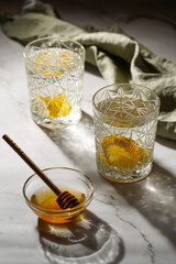 Two glasses with water and lemon, honey in the morning light - breakfast