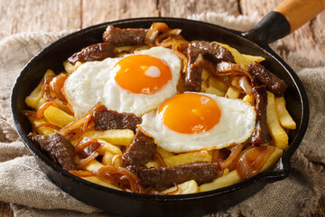 Traditional Chilean Chorrillana made of Fries with beef, caramelized onions, and fried eggs close up in the pan on the table. Horizontal