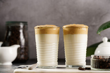 Two glasses with trendy korean beverage dalgona coffee latte - whipped instant coffee, sugar and hot water and milk layers on a marble board, grey surface