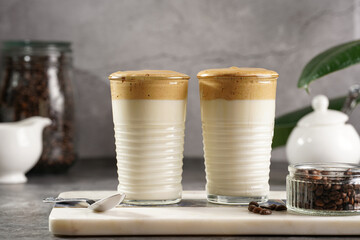 Two glasses with trendy korean beverage dalgona coffee latte - whipped instant coffee, sugar and hot water and milk layers on a marble board, grey surface