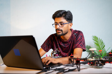 Man or student checking quadcopter or drone by connecting to laptop at laboratory - concept of UAV...