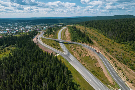 Aerial view of scenic road between green trees with pines on a sunny summer morning. Nature landscape in Siberia, Russia. A road passing through a coniferous forest, aerial shot from a drone.