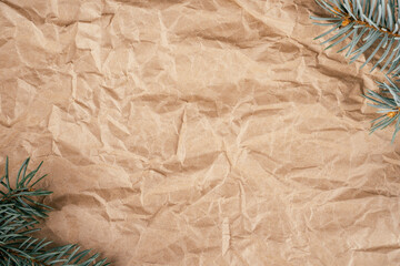 Background image of rough crumpled recycled textured kraft paper with Christmas tree branches. Top view, copy space
