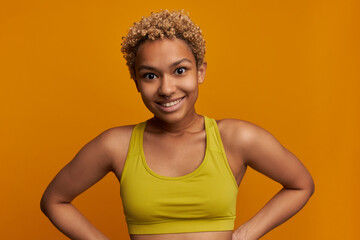 Attractive young athletic female with small blonde poodles and nose piercing posing against orange...