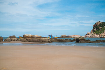 Scenic view of the beach with big stones. Boats sailing on the sea. View of the bay with crystal water. Colourful vietnamese fishing boats.