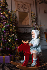 Happy cute beautiful little girl is sitting on a vintage wooden chair-deer with Christmas decorations.	
 
