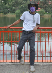 Full length of a young guy standing outside with wearing face mask during covid-19 with looking at camera 