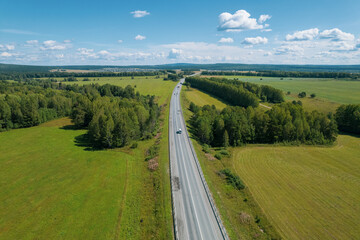 Aerial view of scenic road between green trees with pines on a sunny summer morning. Nature landscape in Siberia, Russia. A road passing through a coniferous forest, aerial shot from a drone.