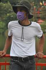 A Indian young man standing outside with wearing boonie hat, white t-shirt and face mask during...