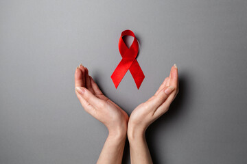 Female's hands frame a red ribbon, a symbol of the fight against AIDS. Gray background. Flat lay. Copy space. The concept of world AIDS day
