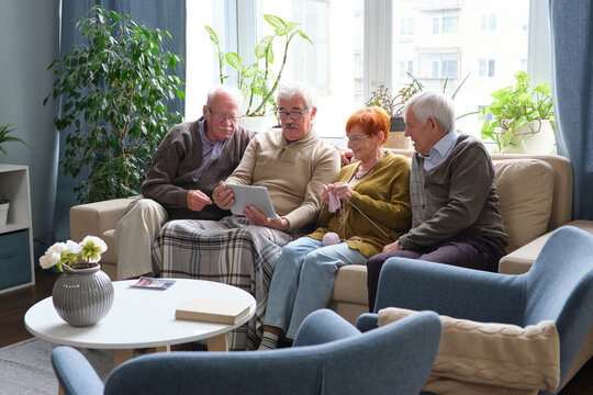 Group of senior friends sitting on sofa together and watching movie on digital tablet in the living room