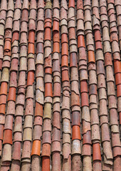 Vertical close-up of old weathered red and orange roof tiles.