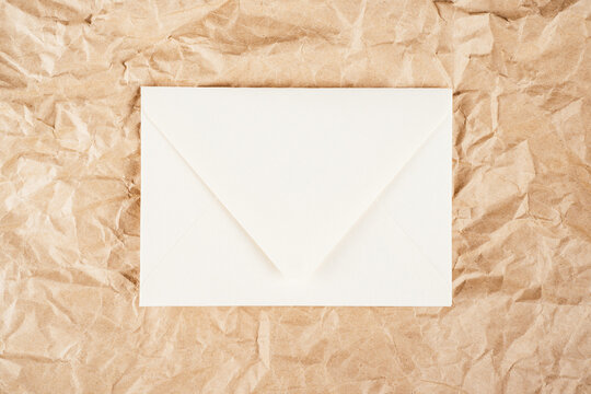 Background image crumpled recycled textured kraft paper with white cardboard envelope in middle. Top view, copy space