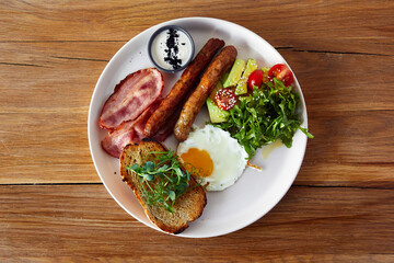 Breakfast with fried sausages, egg, ham, sausages and avocado and tomato salad