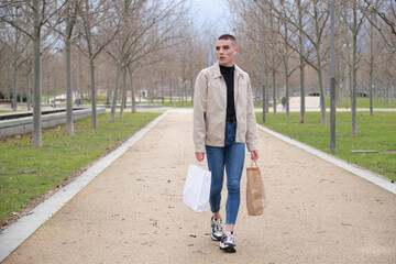 Young man wearing make up walking with shopping bags and listening music.