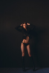 young beautiful girl, model appearance in a black bikini, high boots on her legs, in the studio on a black background