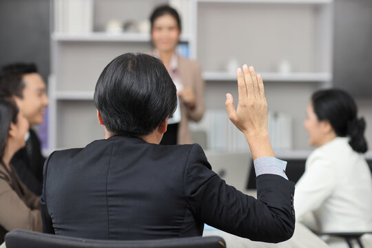 Rear view volunteer man or  businessman raising hand during training seminar presentation at conference boardroom