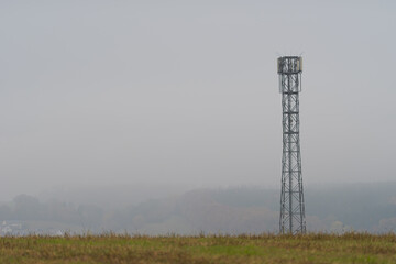 Mobile cell tower antenna mast providing mobile internet connection for rural area standing on empty barren field on grey overcast dark moody day