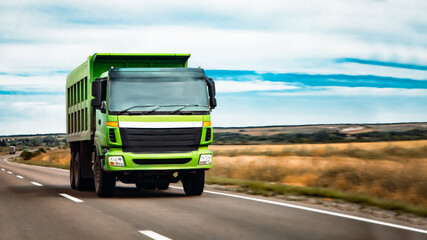 green truck rushes along country road against background of field from road perspective.