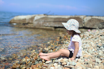 dark blonde girl in a white dress sits on a rocky beach by the sea