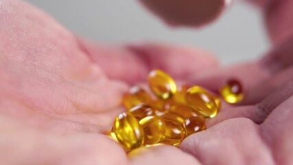 Falling soft gel omega 3 capsules into the palm with wrinkled dry skin from a white pill container. Slow motion. Macro shot. Natural supplements concept. Body care idea - Powered by Adobe