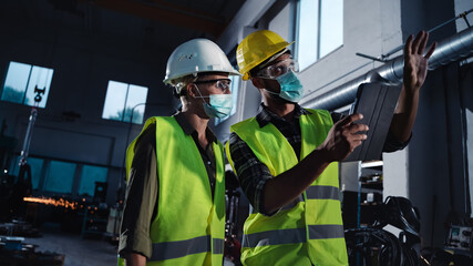 Industrial inspectors with face masks doing general check up at metal workshop, coronavirus concept