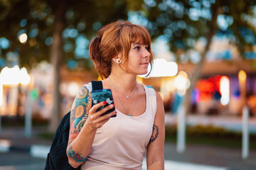 Portrait of a young tanned woman with a tattoo holding a phone in her hand. In the background, the...