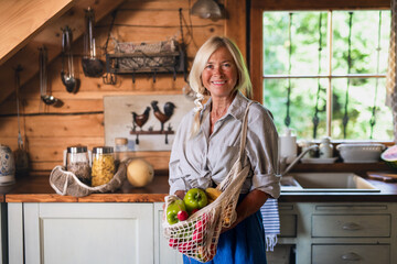 Happy senior woman unpacking shopping indoors at home and looking at camera, sustainable lifestyle.