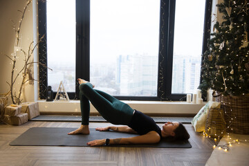 young woman stretching and doing yoga fitness exercise  in the Christmas interior  at home. home fitness, activewear. Healthy and sport lifestyle. Christmas holidays
