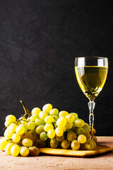a brush of white grapes on a cutting board in the background a glass of white wine on a black background