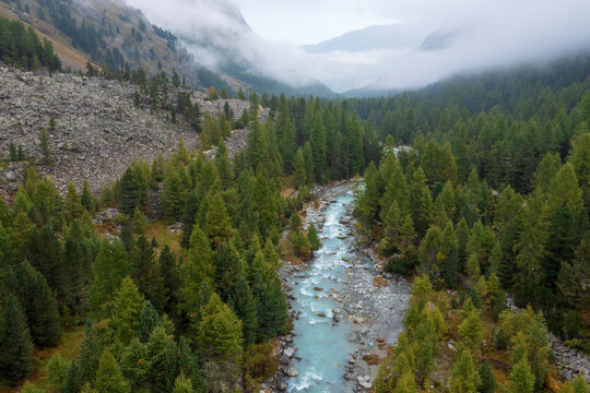 Drone view of Ova da Morteratsch river flowing through Val Morteratsch with thick fog in background