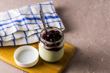 a jar of yogurt with cherry jam on a cutting board next to a towel