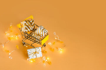 Online christmas shopping and sale. Shopping cart with gift boxes on golden background with lights. Supermarket trolley full presents. Copy space