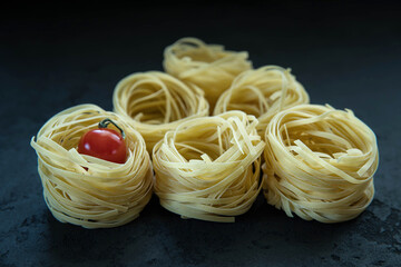 Raw tagliatelle pasta  and tomato on the black concrete background