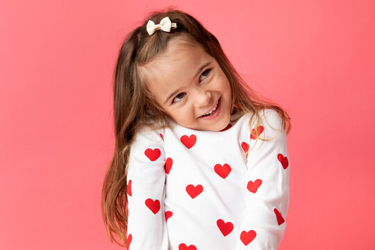 Little girl on pink background making cute shy smile