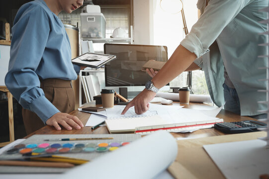 Architects and interior designers woman discussing about concept of building design. Estimation for construction project with material sample, Drawing and Model on desk. Selective focus center image