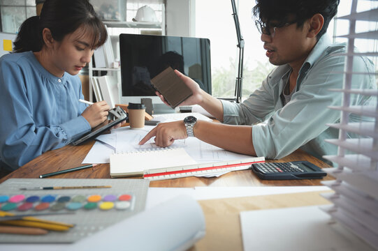Architects and interior designers woman discussing about concept of building design. Estimation for construction project with material sample, Drawing and Model on desk. Selective focus center image