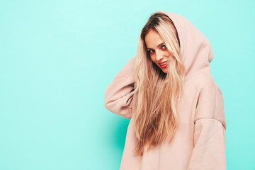 Young beautiful smiling female in trendy summer hoodie. Sexy carefree woman posing near blue wall in studio. Positive blond model having fun and going crazy. Cheerful and happy
