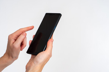 Phone in female hands. Smartphone in hand close up. Girl points her finger at screen. Mobile gadget on light background. Copy space on black screen of phone. Modern Cellphone with dark display
