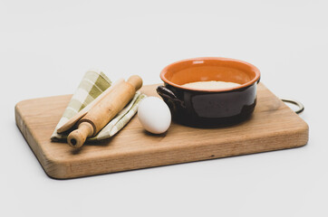 chopping board terracotta bowl with flour wooden rolling pin and white eggs  on a white tabletop
